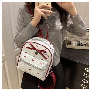 Dettaglio di mini zaino bianco con stampe a fiocchi rossi e ciondolo metallico a cuore