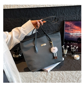 Détail d'un sac cabas gris texturé avec anse noire et breloque pelucheuse blanche