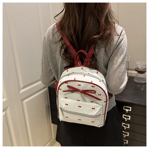 Vista dettagliata del mini zaino bianco con stampe di fiocchi rossi e spallacci in pelle