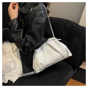 Detail of white woven cloud bag with pleats and thin strap worn by model in leather jacket