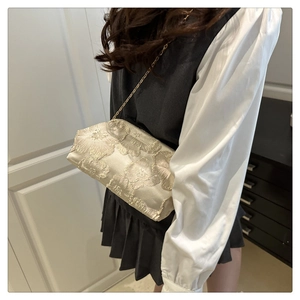 Close-up of champagne silk embroidery detail and delicate gold chain on small evening bag