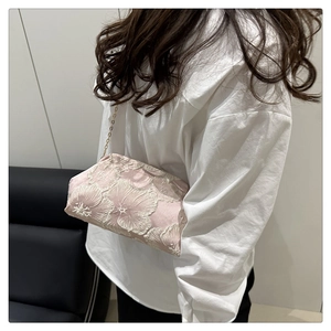 Detail of pink satin evening bag with white floral embroidery and gold chain strap