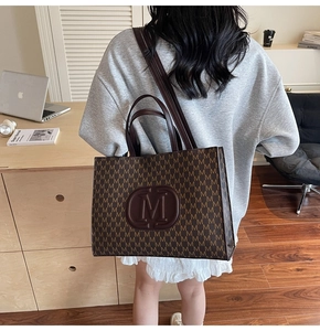 Détail du cabas marron avec imprimés de lettres M et bandoulière dans un bureau chic