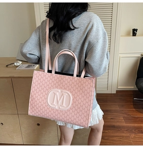 Close-up of pink tote bag with embossed M logo and monogram pattern on premium material