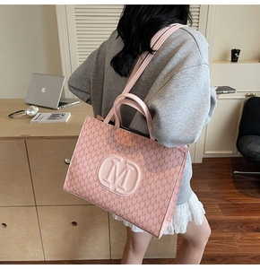 Détail d'un sac cabas rose avec motif à lettres M et logo circulaire dans un cadre lifestyle