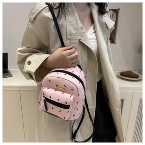 Pink mini backpack detail with bow patterns and fashion metal logo shown on beige coat