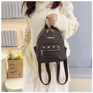 Détail d'un sac à dos marron à motifs avec fermetures éclair dorées tenu par mannequin