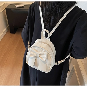 Rear view of a model wearing the cream bow-knot mini backpack in a minimalist room