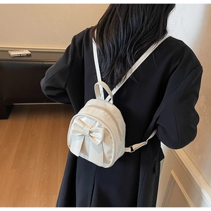 Close-up of a mini cream bow backpack on a model wearing a black winter coat