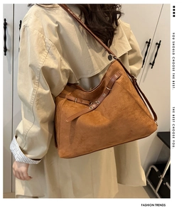 Gros plan du sac fourre-tout en daim marron avec boucles porté sur un trench beige