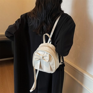 Chic white mini backpack with large bow detail shown on black coat for high contrast