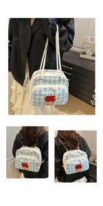 Detail of blue plaid canvas bag featuring a red apple print and versatile shoulder straps