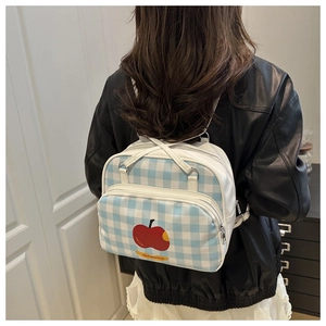 Detail of blue and white checkered backpack featuring red apple prints and slim white straps