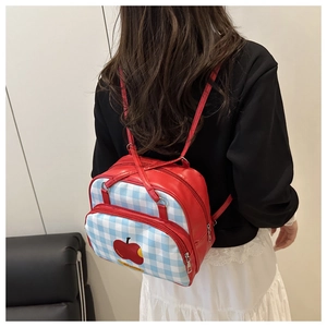 Detail of red leather and blue checkered backpack featuring a cute apple patch
