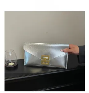 Detail of silver envelope clutch featuring metallic texture and golden geometric buckle clasp