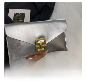Silver crosshatch leather envelope clutch bag with gold clasp held against a magazine