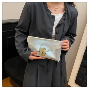 Silver envelope clutch bag with gold rectangular clasp held against a grey suit