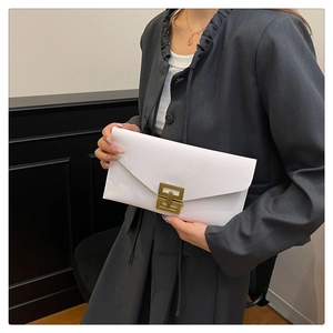 Detail of white leather clutch with gold geometric clasp held by model in suit