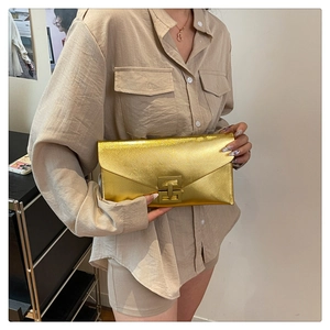 Close-up of golden envelope clutch with metallic lock held by a model in soft lighting