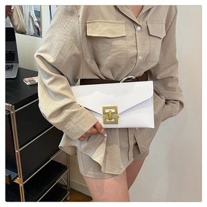 Macro detail of a white envelope clutch bag featuring a gold geometric metal buckle
