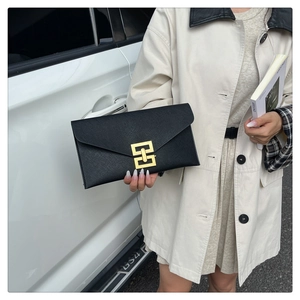 Close-up of black envelope clutch with golden geometric clasp and cross-grain texture