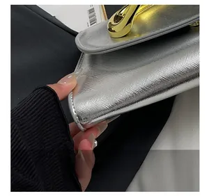 Détail d'une pochette en cuir argenté avec coutures de précision et garniture dorée
