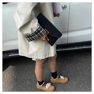Close-up of a black minimalist envelope bag with gold buckle held by a stylish model