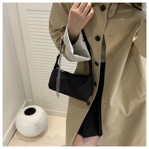 Sac sous le bras en nylon noir avec chaîne argentée porté sur un trench-coat beige