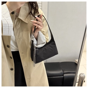 Gros plan du sac baguette en nylon noir avec chaîne argentée porté sur un manteau