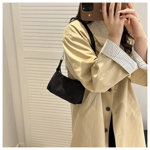 Détail d'un sac demi-lune en nylon noir avec chaîne argentée porté sur un trench beige