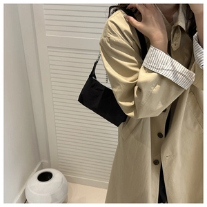 Sac à bandoulière en nylon noir avec chaîne porté par un mannequin en trench-coat beige