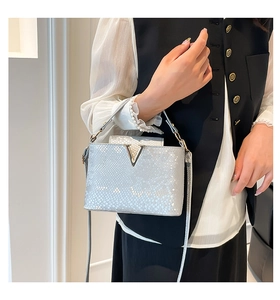 Detailed view of silver snake skin texture handbag with V-shaped metal logo and leather strap