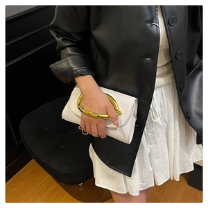 Gros plan d'un sac à main en cuir blanc avec poignée en métal doré porté par un mannequin