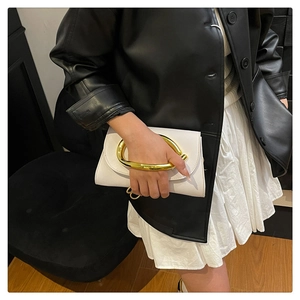 Gros plan d'une pochette en cuir blanc avec poignée incurvée en métal doré sur un modèle