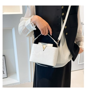 Detail view of white snakeskin texture bucket bag with golden V-shaped buckle hardware