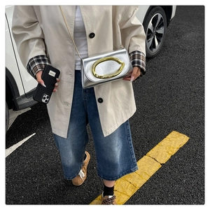Sac bandoulière argenté à boucle dorée porté par un mannequin en trench-coat chic