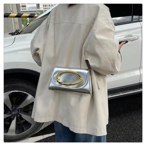 Détail du sac argenté à chaîne avec boucle dorée porté par un mannequin en extérieur