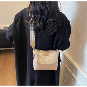 Detail of quilted beige shoulder bag featuring wide V-pattern fabric strap and fashion label