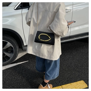 Gros plan sur un sac de soirée en cuir noir avec boucle ovale dorée et bandoulière