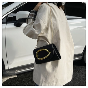 Detail of a black leather evening bag featuring a large gold sculptural metal buckle