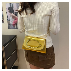 Détail du sac bandoulière doré métallisé porté avec un pull blanc et jupe en daim