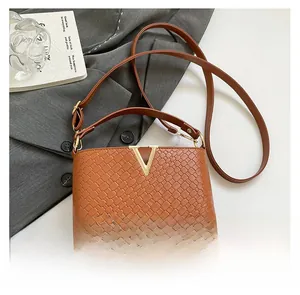 Detail of woven texture and gold V-shaped buckle on brown leather crossbody bag