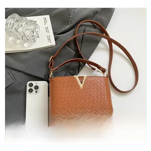 Detailed view of brown woven texture handbag with golden V buckle and slim strap