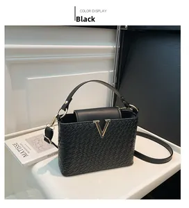 Detail of black woven texture handbag featuring a gold V-shaped logo and round handle