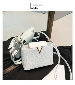 Close-up of white woven leather handbag with gold V hardware on black silk background