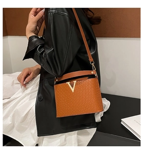 Brown leather bucket bag with woven texture and gold V-shaped metal logo shown on model