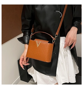 Detailed shot of a brown crocodile texture bucket bag with metal V logo and shoulder strap