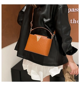 Detail of a brown crocodile texture handbag with a vintage metal V logo and shoulder strap