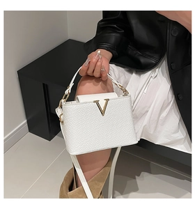 Detail view of white woven texture crossbody bag with gold V logo and metal hardware