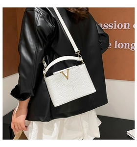 Detail showing white crocodile pattern handbag with gold V-shaped logo and slim strap
